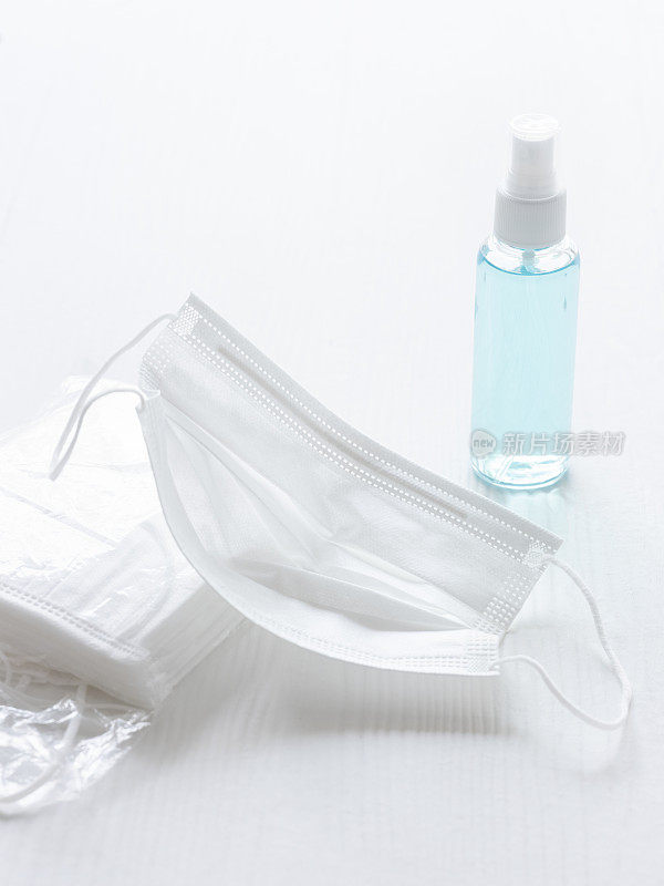 外科口罩，旁边是一包口罩和一瓶洗手液，在白色的桌子背景上，选择聚焦，聚焦在前景的口罩上。