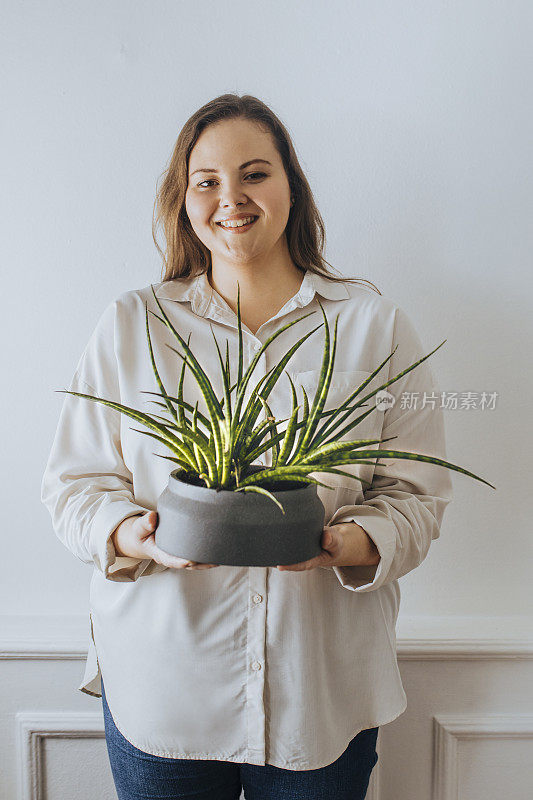 腰上的肖像，一个快乐的加码女人拿着一种房子植物看着相机