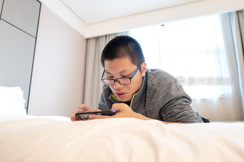 一个年轻人在旅馆的床上玩手机