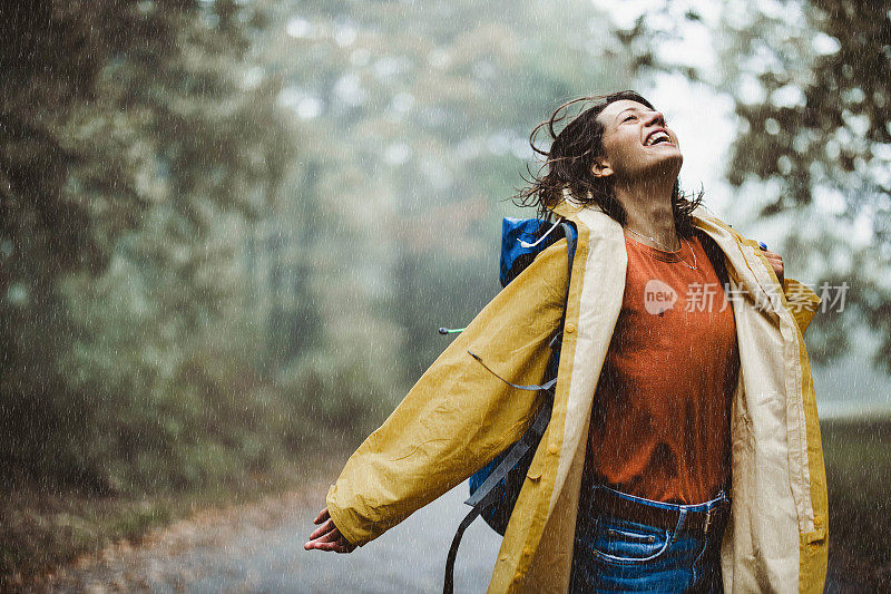 穿着雨衣在公园里享受雨的快乐女人。