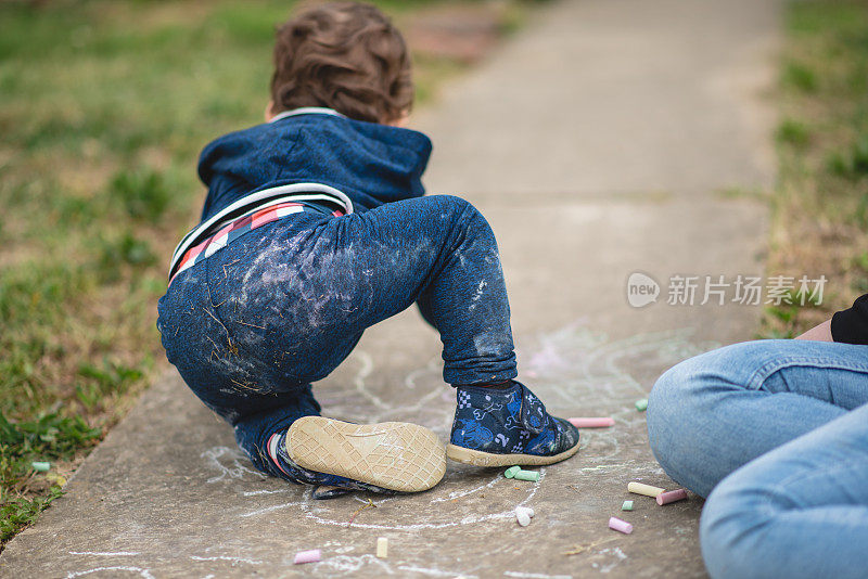 蹒跚学步的小男孩和他的妈妈玩，用粉笔在地上乱画