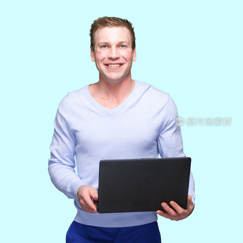 白人男性穿着v领，站在有色背景前使用笔记本电脑