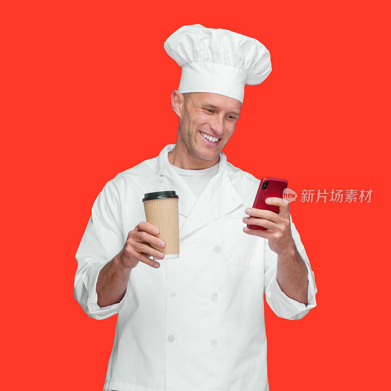 白人男厨师穿着制服站在有色背景前，拿着咖啡杯，发短信