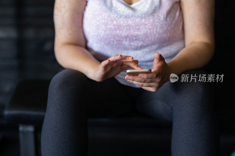 锻炼休息:一个超重的女人在健身房使用她的手机