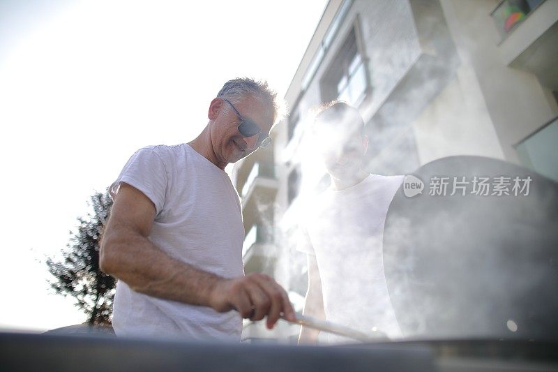 和家人在后院里享受烧烤，烧烤上的荤菜，父子俩在花园里烧烤