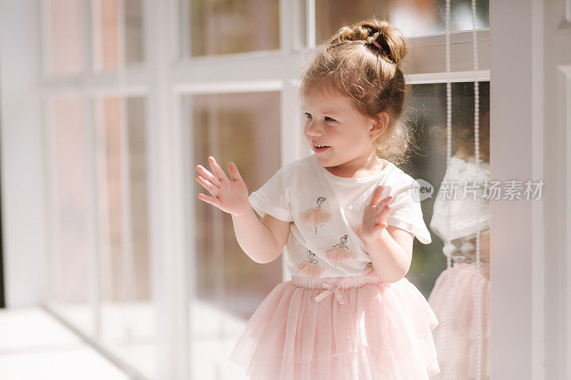 可爱的三岁小女孩穿着衣服摆姿势拍照在工作室。漂亮的小女孩坐在窗台上