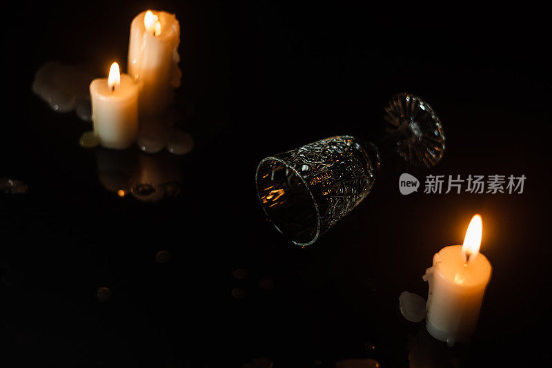 打翻的水晶玻璃放在蜡烛之间的暗色镜子桌上。宴会的概念