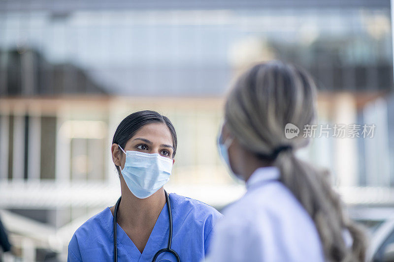 年轻的女医生戴着口罩在医院外面和同事交谈