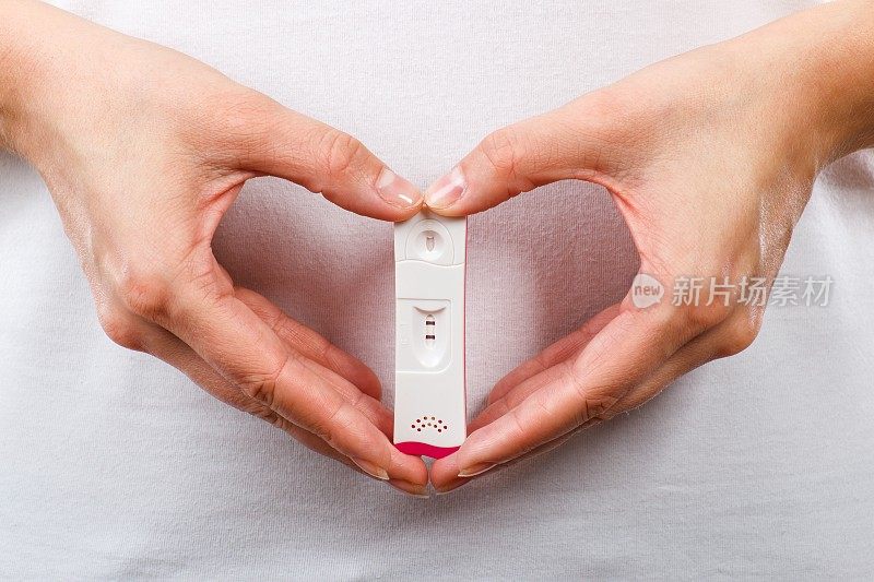 心脏形状妇女的手拿着妊娠试验结果为阳性