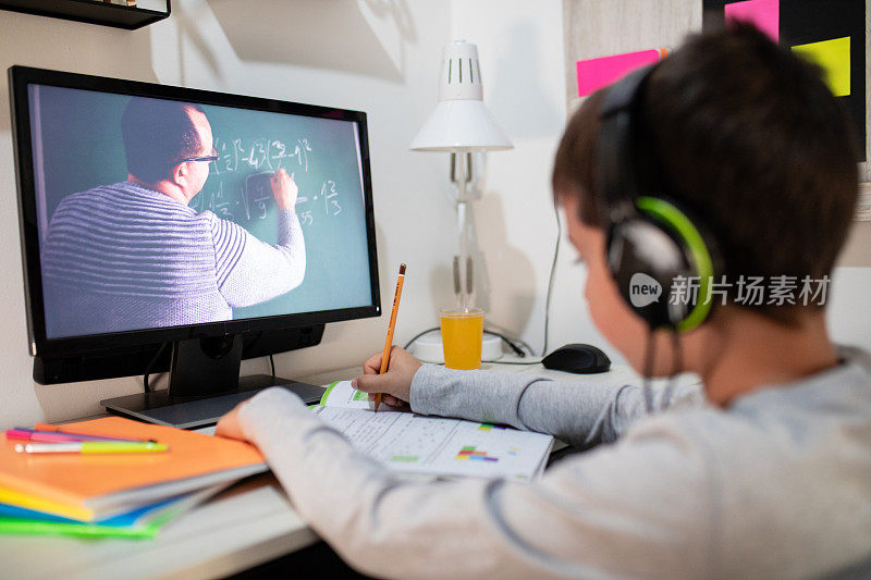 远程学习中，一个男孩戴着耳机坐在家里的桌子旁。理念线上教育、家庭教育、科技、学校