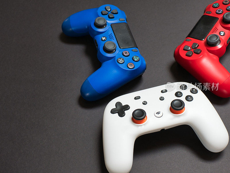 三个游戏控制器在白色，蓝色和红色，在黑色的背景。聚焦于白色控制器