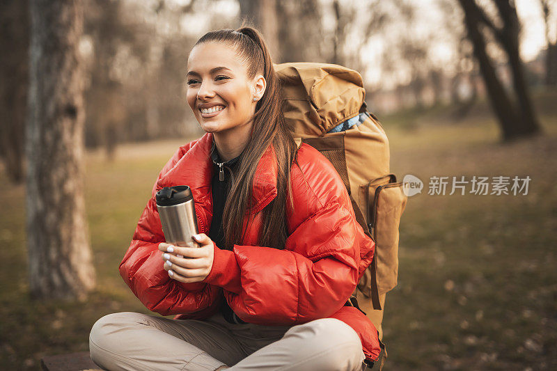 美丽的年轻女子喝着咖啡，在山间徒步旅行时休息一下