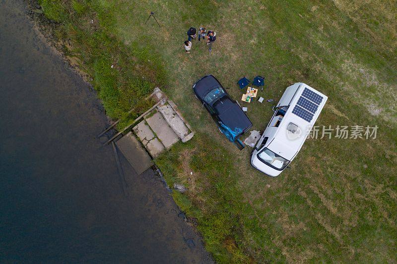 露营车房车与太阳能电池板无人机航拍两对夫妇生活在河边和草地在葡萄牙日落