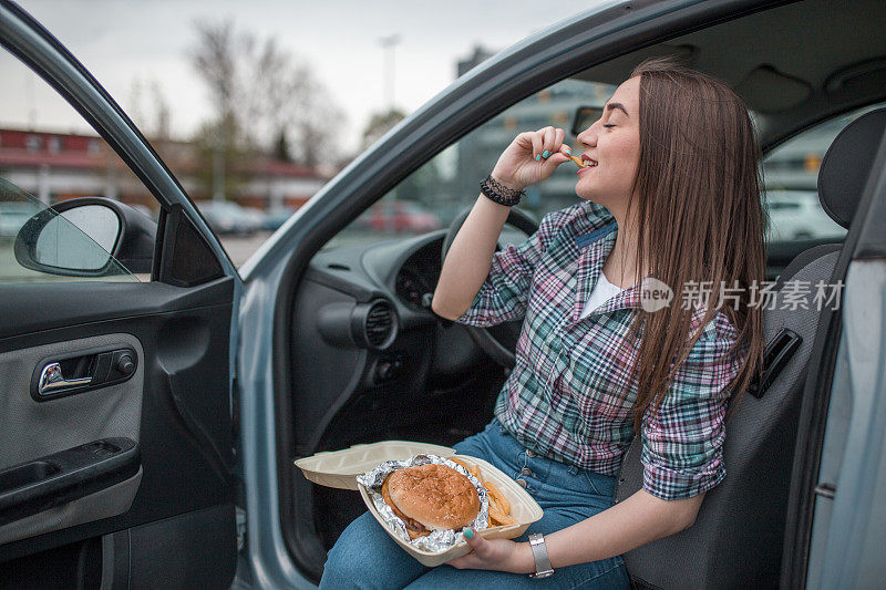 可爱的女人在车里吃汉堡和薯条