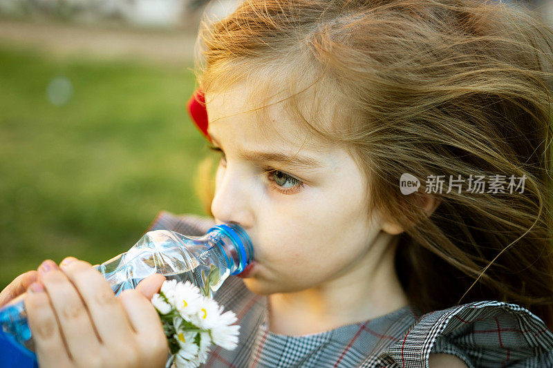 美丽的小女孩正在喝瓶子里的干净水。炎热的夏天