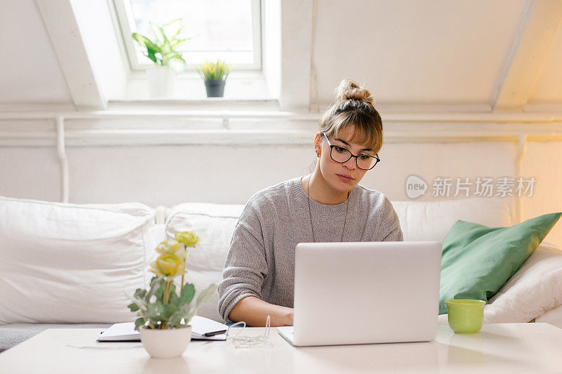 漂亮的年轻女子坐着用笔记本电脑做作业