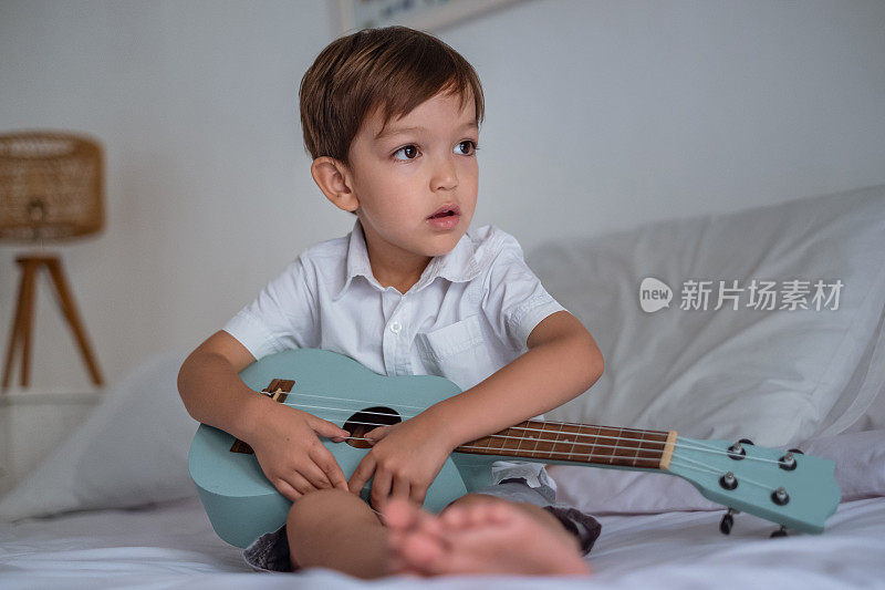 小男孩在床上弹尤克里里吉他