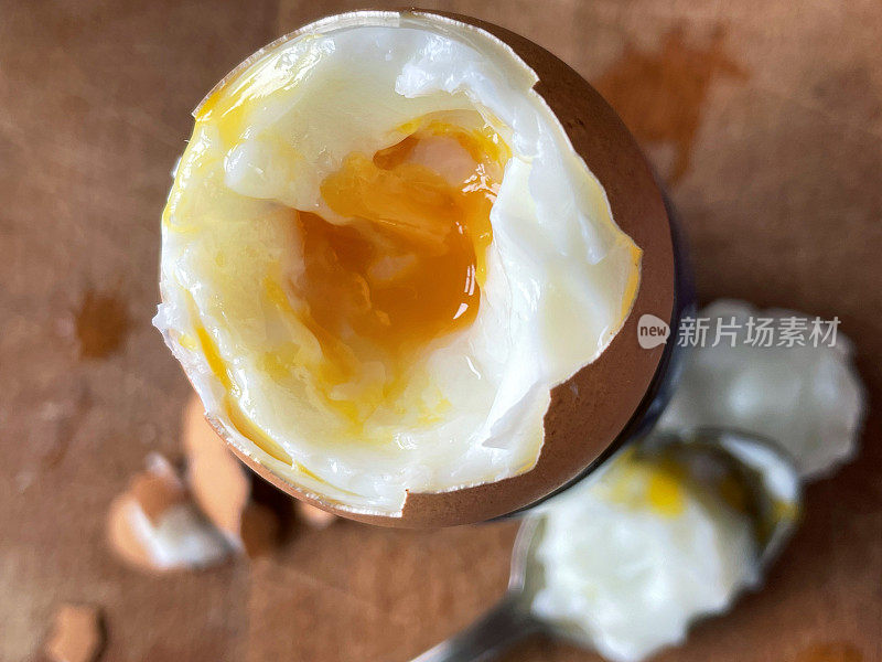 木制切菜板上的瓷蛋杯里的溏心蛋图像，剥去蛋壳和顶部显示流的蛋黄，升高的视野