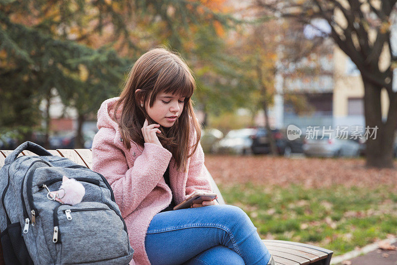 一个严肃的十几岁女孩独自坐在公园长凳上发短信