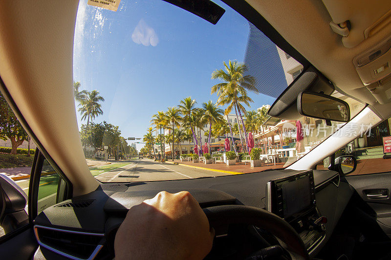 视角拍摄的一个年轻的运动男子驾驶汽车在迈阿密海滩地区的天堂蓝色的海洋景观，迈阿密，南佛罗里达，美国-美国