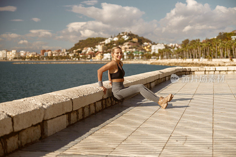 微笑的年轻女运动员在海边做热身运动