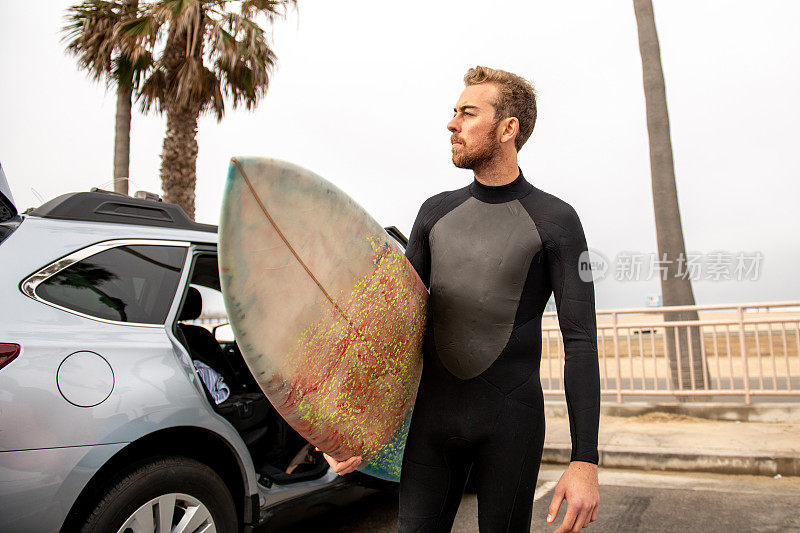 冲浪者站在车旁边拿着他的冲浪板