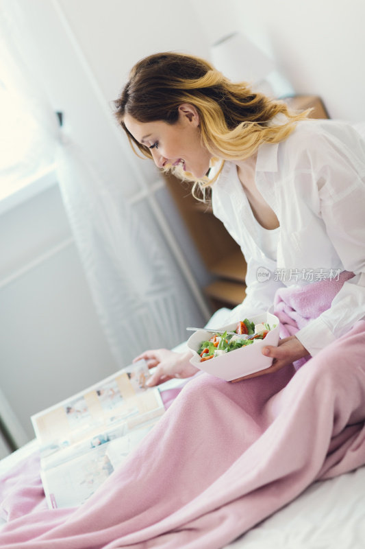 女人在床上吃健康早餐和看杂志。