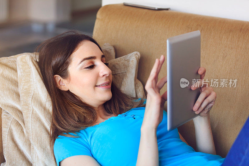 快乐的年轻女子躺在沙发上用平板电脑