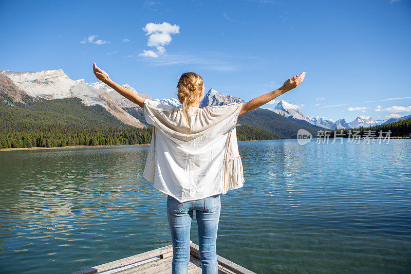 湖边的一位年轻女子正张开双臂寻求积极的情绪。