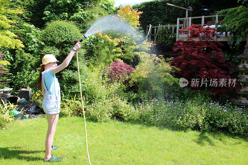 女孩用软管浇灌花园草坪的形象