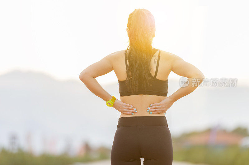 运动的年轻女子在慢跑后摩擦下背部肌肉