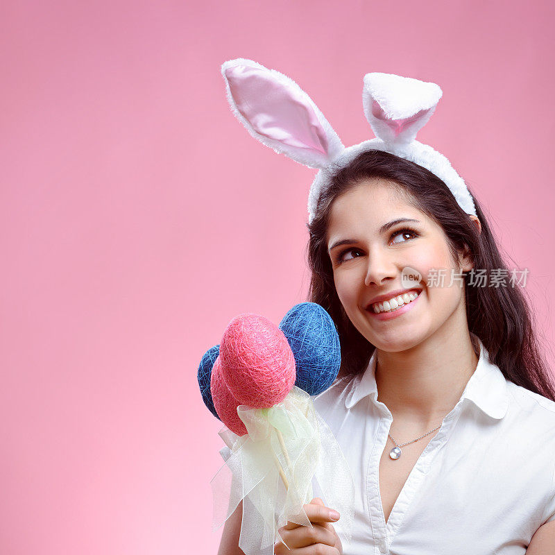 漂亮的年轻女人戴着兔子耳朵拿着复活节彩蛋