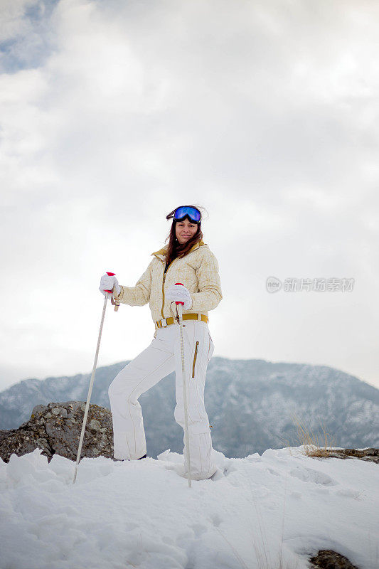 近景美丽的年轻女子在冬天的衣服站在一边，手拿木棍的背景雪山