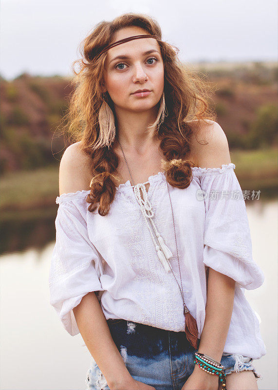 一个可爱的波西米亚风格的女孩的肖像在一个湖的背景。柔和温暖的复古照片颜色。