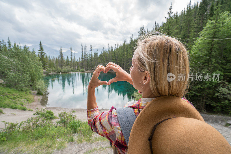 年轻女子在山湖上做心形手指架