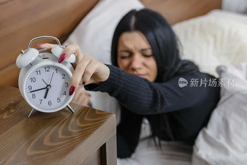 闹钟。早上，一个女人躺在床上用手关掉闹钟