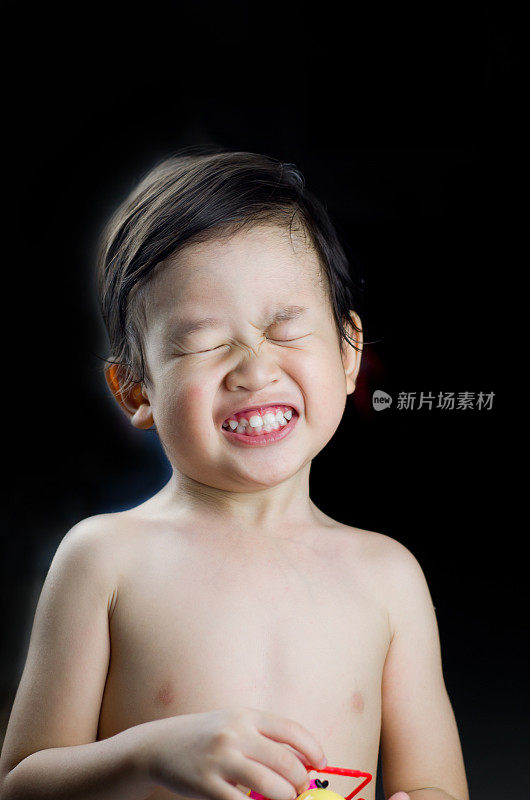 表情可爱的亚洲婴儿微笑或快乐的婴儿脸与玩具在黑色的背景，童年概念，幸福的家庭概念