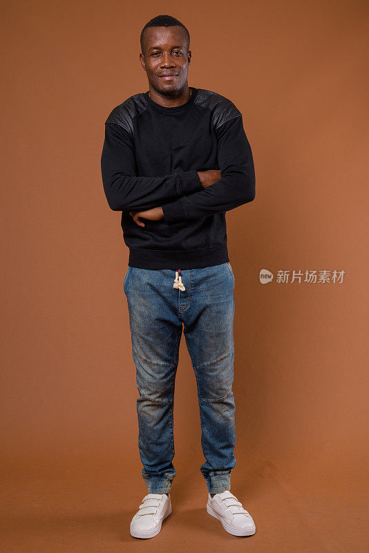 工作室拍摄的肌肉发达的非洲男子穿着黑色长袖衬衫，背景是彩色的