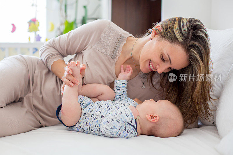 年轻的母亲，躺在床上和她刚出生的男婴玩耍