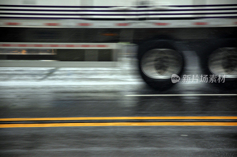 雨水从移动的卡车车轮上喷射。城市道路在大雨中