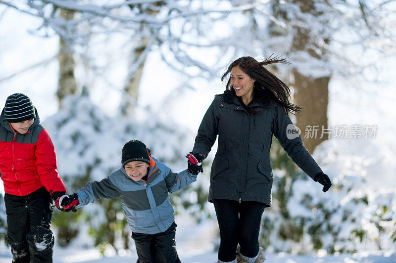 一位年轻的妈妈和她的儿子们在雪中玩耍