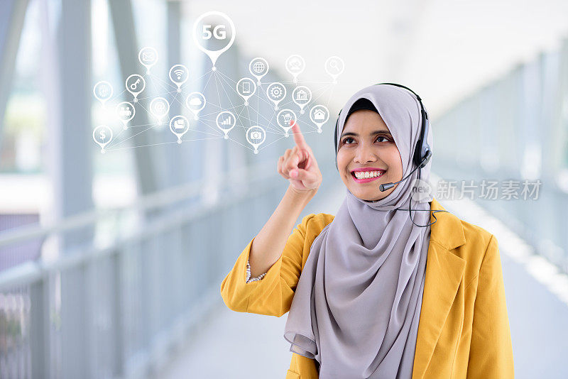 年轻的穆斯林女商人戴着头巾和耳机使用5G
