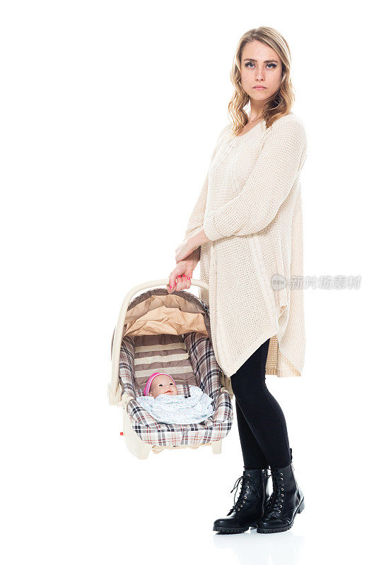 年轻漂亮的妈妈穿着毛衣抱着婴儿汽车座椅，真严肃
