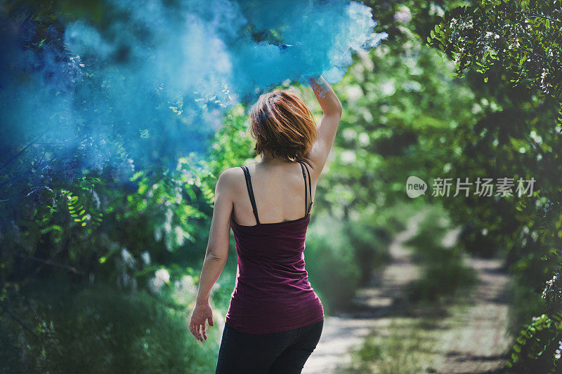 在大自然中拿着蓝色烟雾弹的女人。
