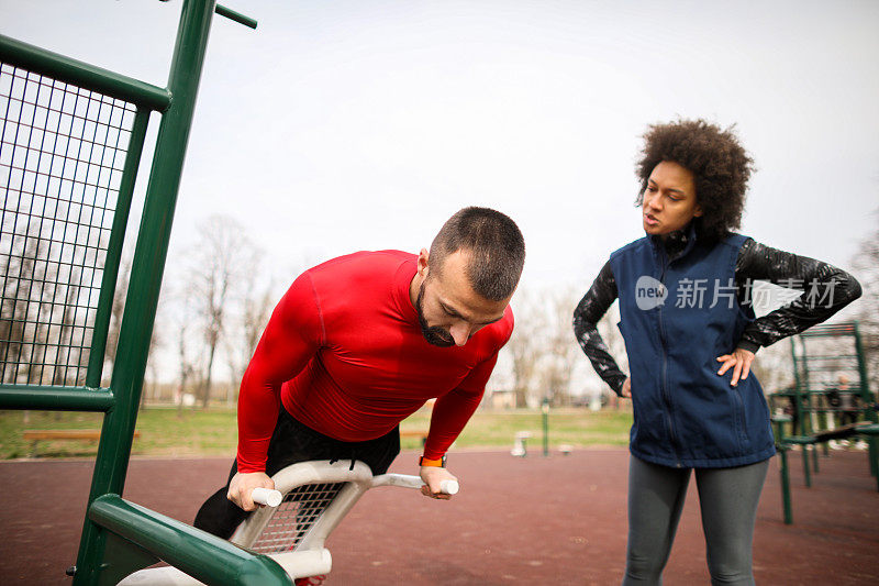 私人健身教练在一个公园健身设备上向一名年轻的女运动员展示锻炼计划