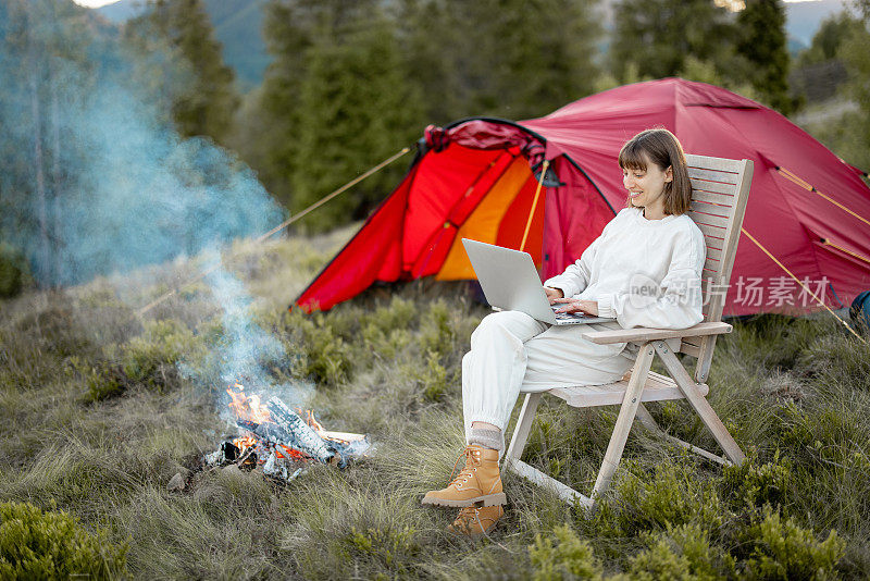 她坐在山间的篝火旁，在笔记本电脑上轻松地工作