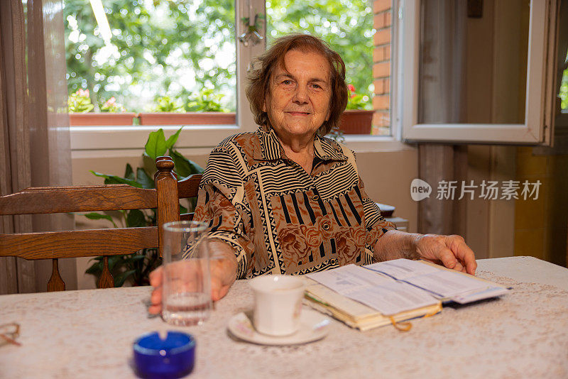 开朗的老年高加索妇女的肖像，94岁，坐在桌子和阅读一本书