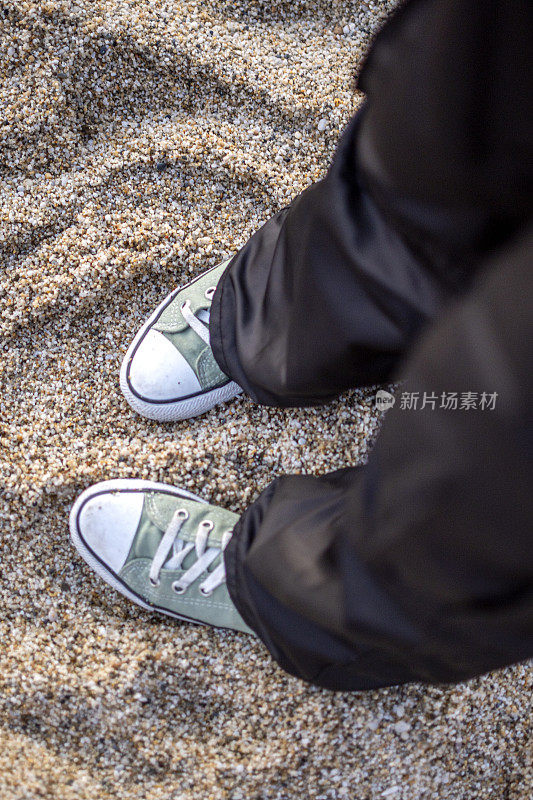 脚有问题。穿着蓝色运动鞋的女性双脚站在卵石滩上