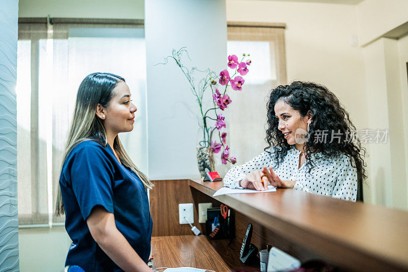中年成年妇女在牙科诊所的接待处与接待员交谈