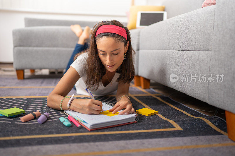 年轻的女学生，躺在客厅的地毯上，在笔记本上写着什么